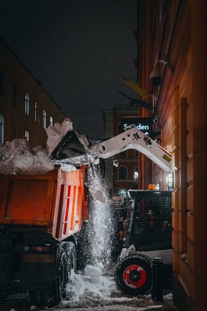 The Art of Drawing Readers In: Your attractive post title goes here An excavator loads snow into a truck on a city street during nighttime winter clearing.