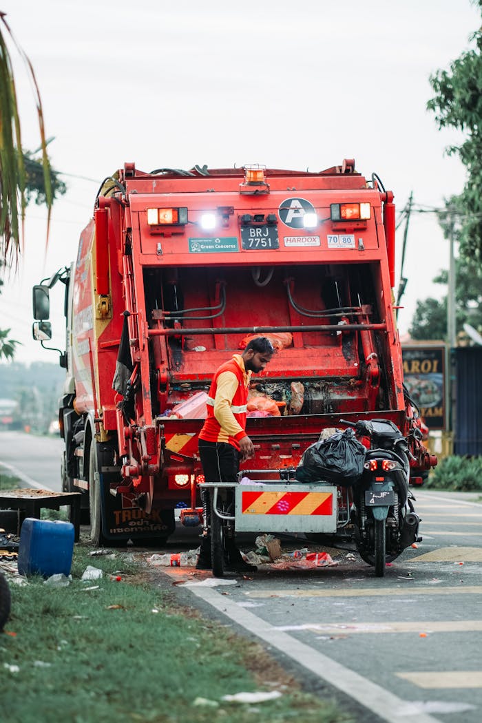 A sanitation worker managing waste disposal behind a garbage truck in Klang, Selangor.
